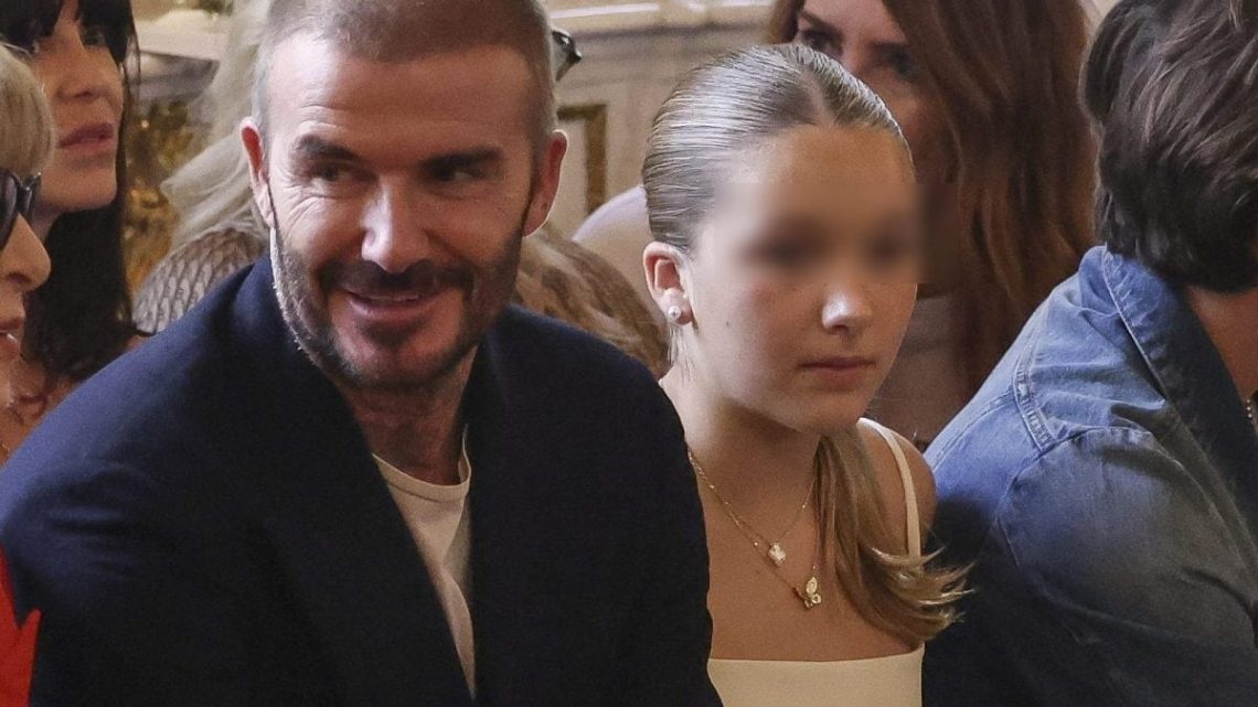 Harper Beckham au défilé de mode à Paris dans une robe blanche et un collier porte-bonheur soutient sa mère Victoria.